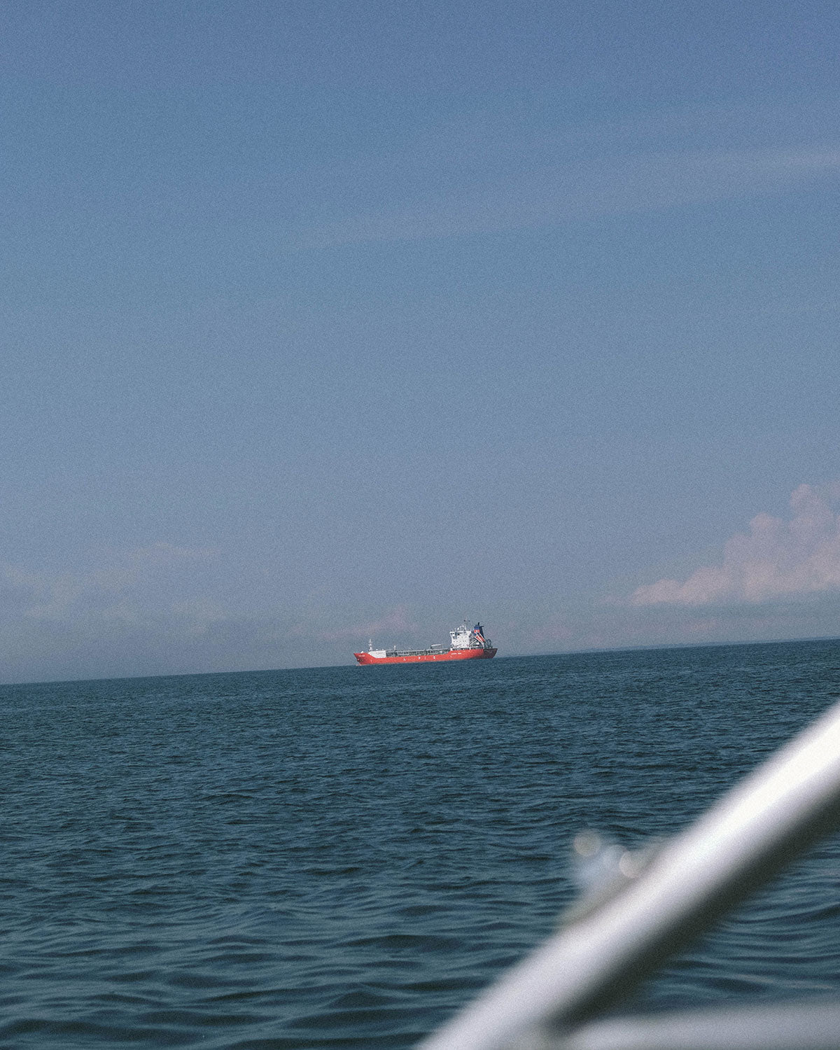 A red cargo ship on the horizon, seen from a boat
