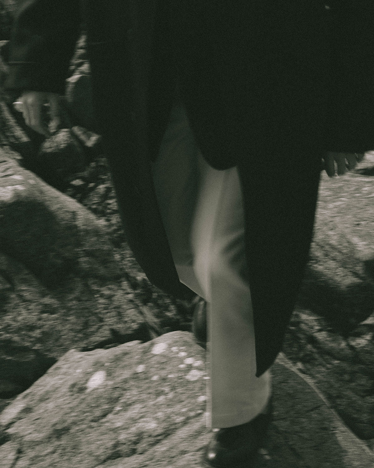 Detail of white trousers and a dark coat stepping over rock, in motion